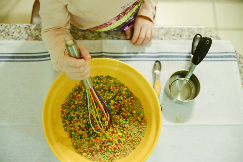 image of a child using a whisk to stir a bowl of brightly colored pulverized cereal.  

 c 