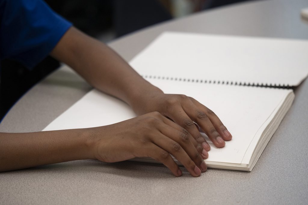 Photo of child's hands reading braille page from book. 