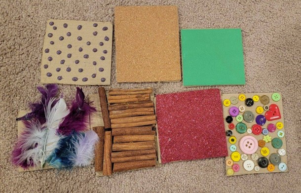 Sensory tiles. From top left: bumpy sensory tile (made with hot glue), cork tile, smooth tile made of craft foam sheet. Bottom left: feathery tile, cinnamon stick, paper tile, button tile.