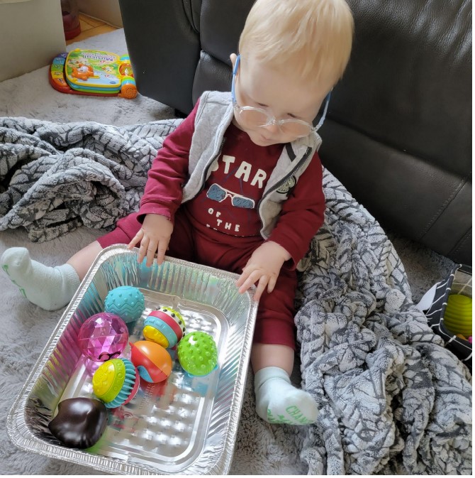 Dominic sitting on the floor with a baking tin with all sorts of balls in it.